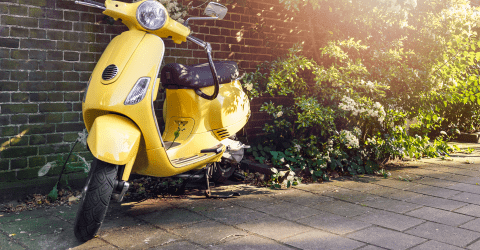 Gele scooter staat geparkeerd bij een muur met struiken op de achtergrond